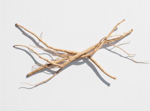 orzenie ashwagandhy o naturalnym kolorze ułożone w krzyż na białej powierzchni.