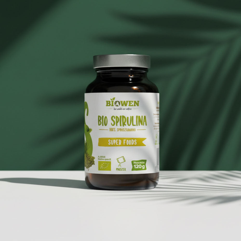  Bio Spirulina Biowen 120 g na białej powierzchni z zielonym tłem.Słoiczek suplementu.