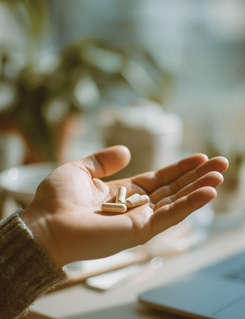 Dłoń osoby trzymająca kilka kapsułek BrainFuel Biowen na rozmytym tle wnętrza