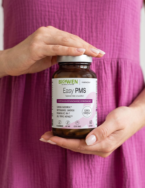Kobieta trzyma suplement diety Easy PMS Biowen w kapsułkach – szklana butelka na tle różowej sukienki, produkt wspierający równowagę hormonalną