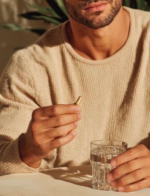 Mężczyzna trzyma kapsułkę suplementu Biowen Kordyceps i szklankę wody