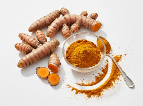 Świeże korzenie kurkumy i miseczka z kurkumą w proszku oraz łyżeczką na białym tle.