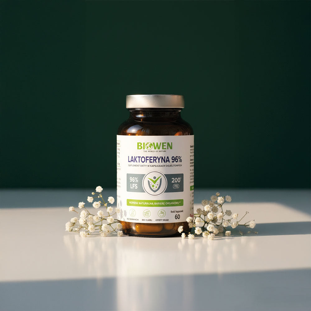 Suplement Biowen Laktoferyna 96% 60 kapsułek ustawiony między drobnymi białymi kwiatami na białej powierzchni.