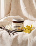Naturalny dezodorant w kremie Biowen 65 g o zapachu wanilii i kwiatów ylang-ylang, otoczony kwiatami i laskami wanilii.
