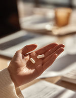 Dłoń osoby trzymająca dwie kapsułki  NeuroShield Biowen na tle dokumentów