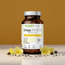 Opakowanie Omega 3-5-6-7-9 Biowen 1520 mg z kapsułkami na jasnej powierzchni z kwiatami i przyprawami na tle żółtego tła