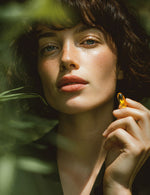 Kobieta w naturalnym świetle trzymająca przy twarzy przezroczystą kapsułkę suplementu Omega 3.