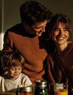 Rodzina z małym dzieckiem uśmiecha się, siedząc przy stole oświetlonym słońcem.