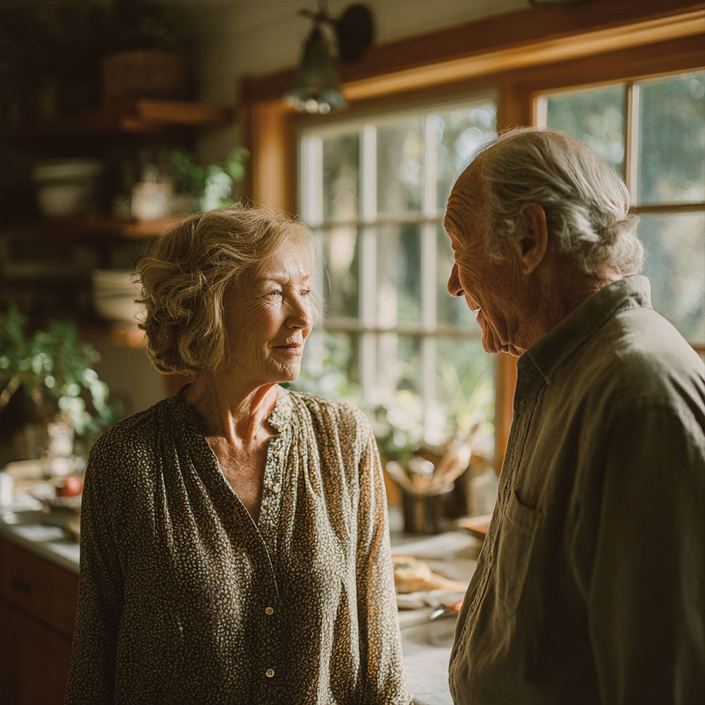 Starsza kobieta i mężczyzna rozmawiający w jasnej kuchni z dużym oknem w tle.