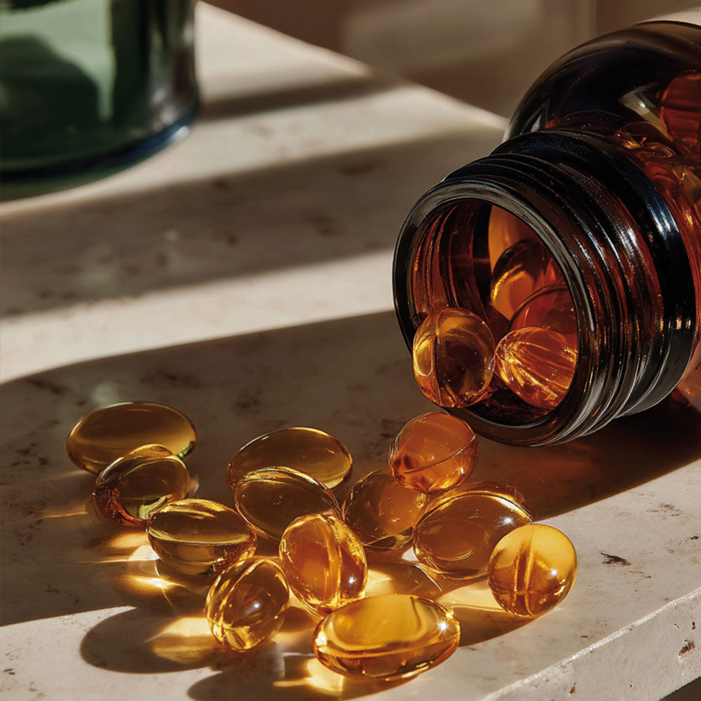 Żółte kapsułki Omega 3 wysypane z brązowego słoiczka na marmurowy blat.