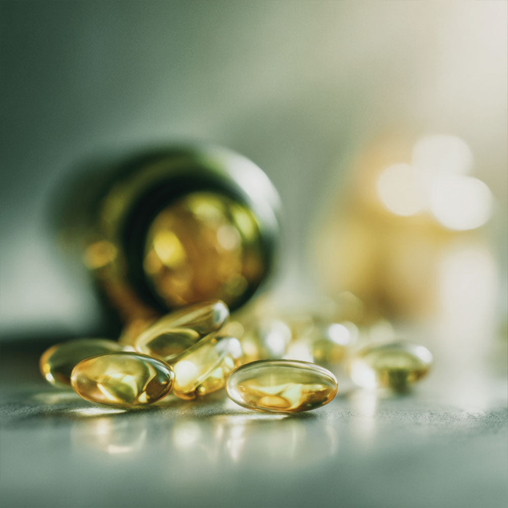 Kapsułki Omega 3 Forte Biowen w bursztynowym odcieniu wysypane z butelki na blat.