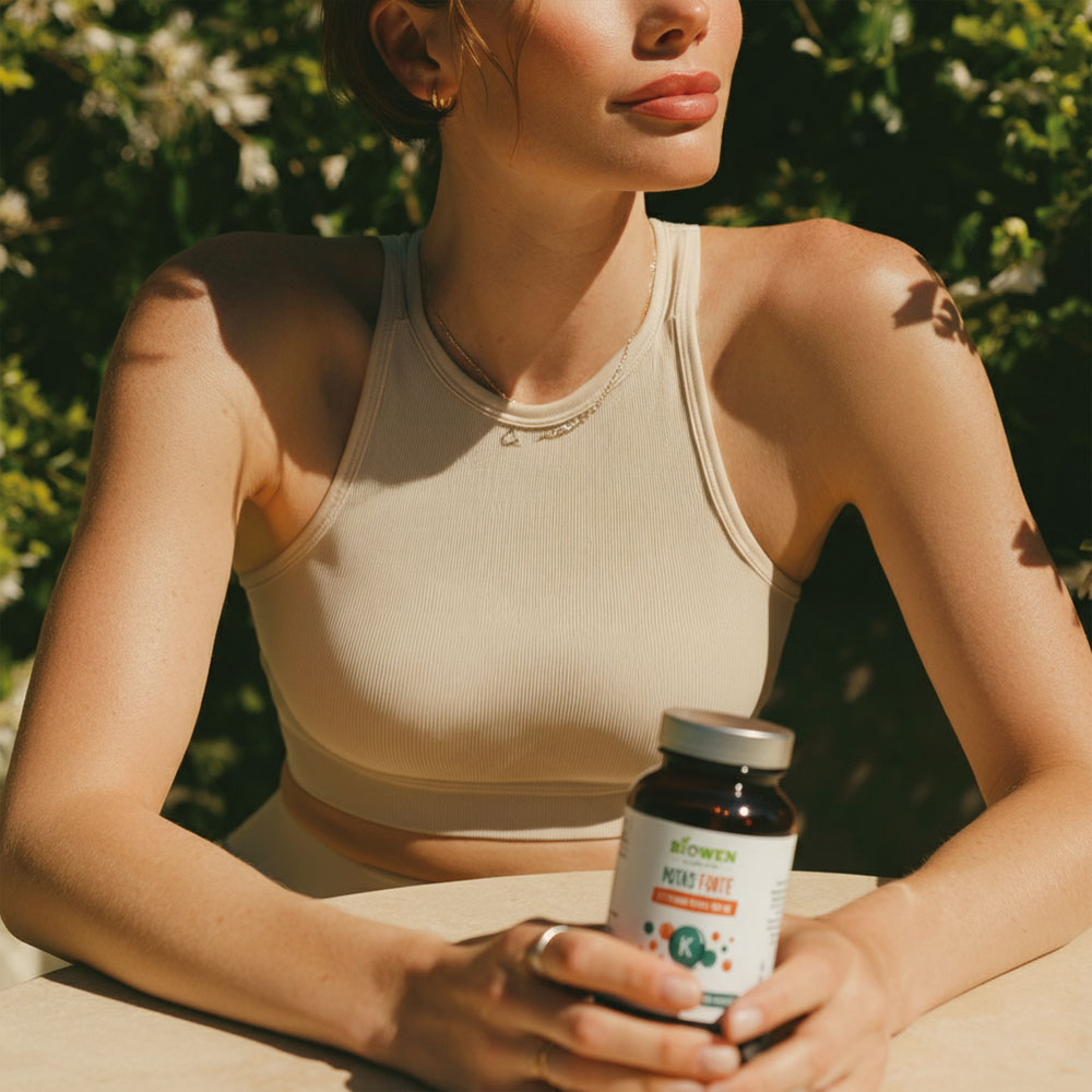 Kobieta trzymająca w dłoni suplement diety Potas Forte Biowen, siedząca przy stole w słoneczny dzień.