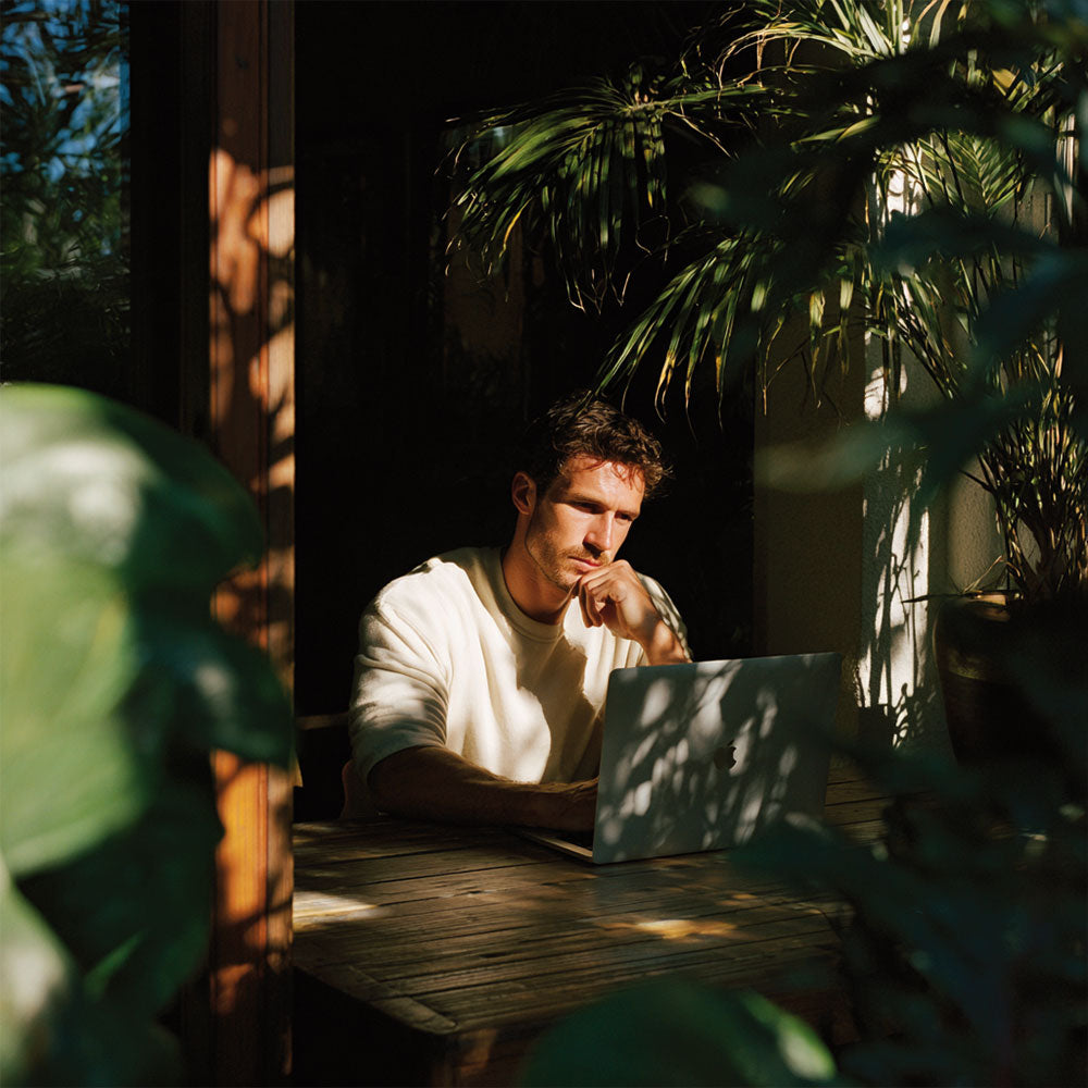 Mężczyzna pracujący przy laptopie przy drewnianym stole otoczonym roślinami