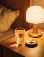 Szklanka wody i dwie kapsułki Sleep Support Biowen na małym talerzyku stojące obok lampki nocnej na stoliku