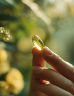 Dłoń trzymająca kapsułkę Witamina D3 + K2 Biowen 90 kapsułek na tle zielonych roślin.