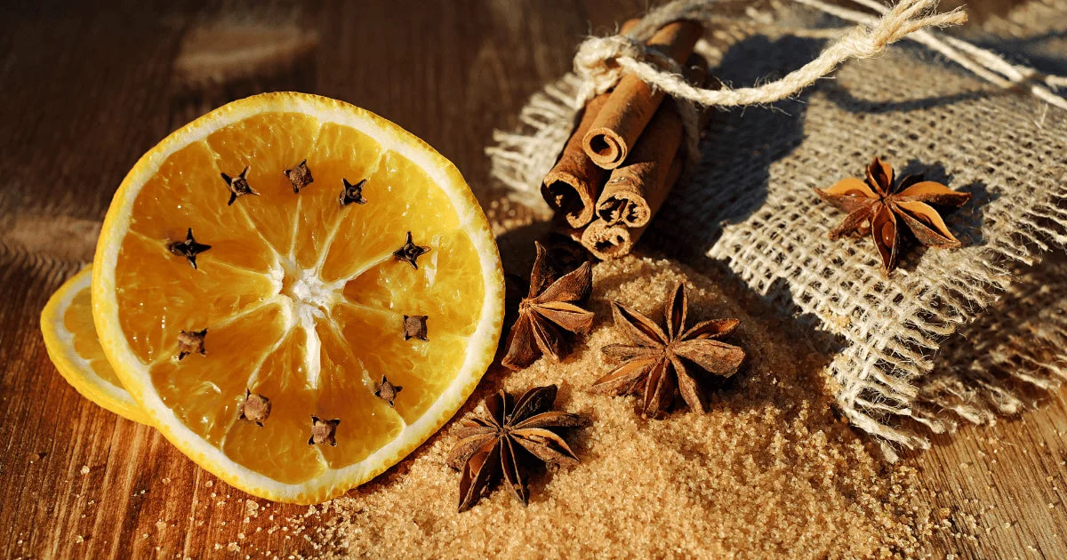 Świąteczna kompozycja: pomarańcza nabita goździkami, laski cynamonu przewiązane sznurkiem oraz anyż gwiazdkowy na brązowym cukrze. Elementy idealne do grzańca.