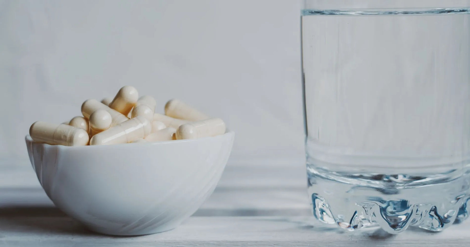 Colostrum w kapsułkach w białej miseczce obok szklanki wody – suplement wspierający odporność i regenerację.