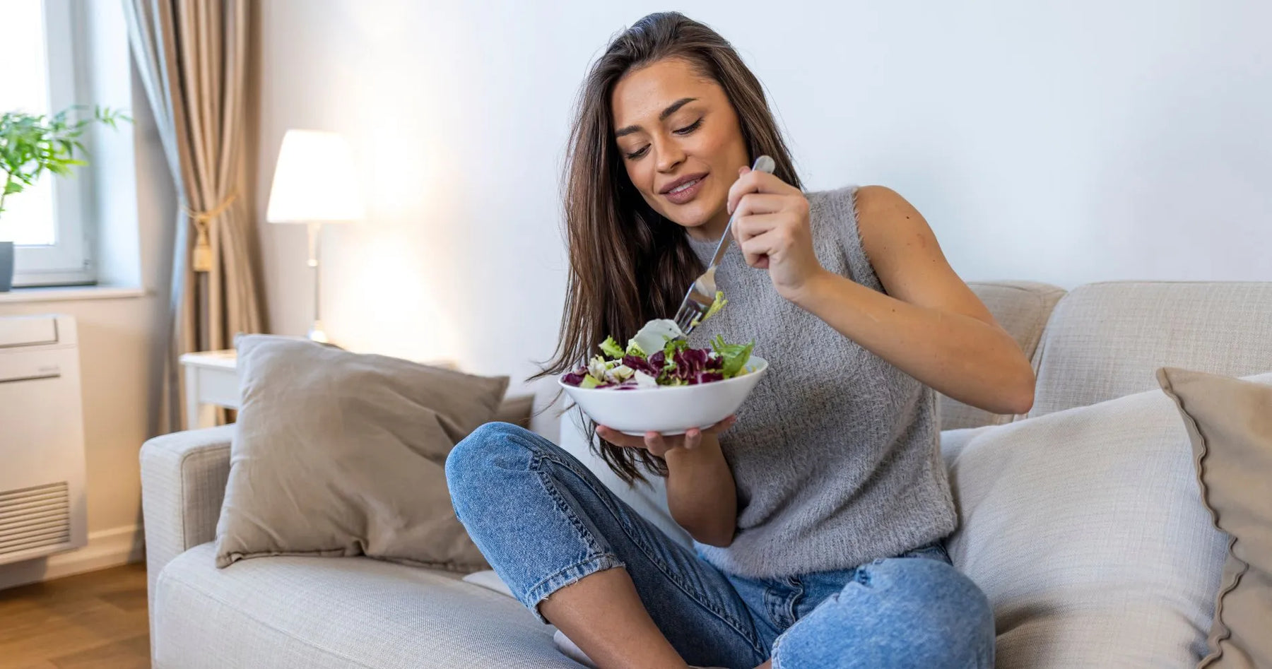 Kobieta jedząca sałatkę na kanapie – przykład zdrowego stylu życia w diecie fleksitariańskiej.