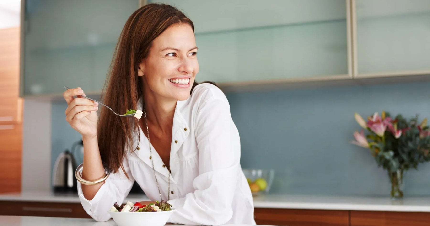 Uśmiechnięta kobieta jedząca lekkostrawny posiłek w kuchni.