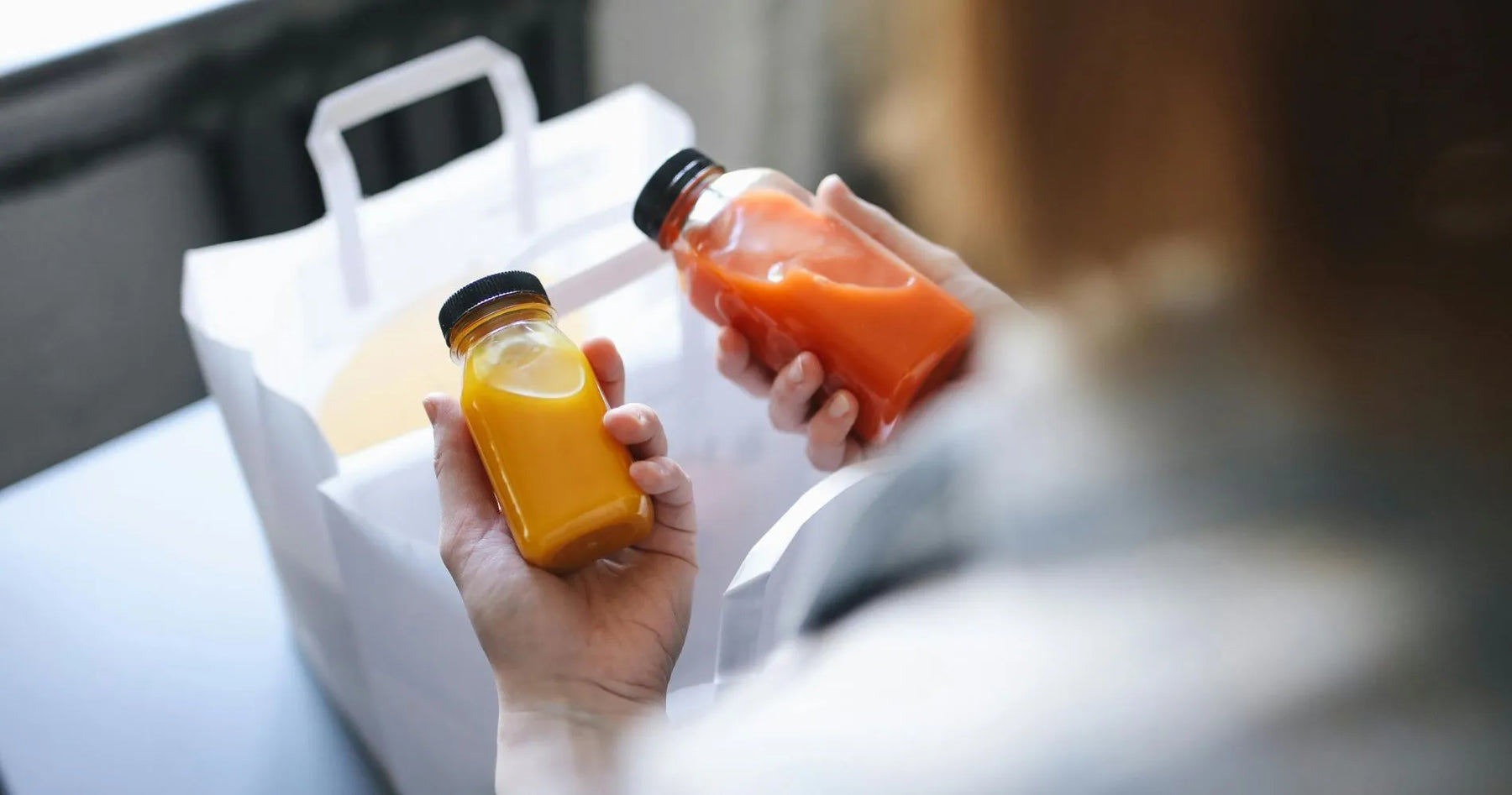 Osoba trzymająca dwie butelki z sokami – pomarańczowym i czerwonym – w ramach diety sokowej.