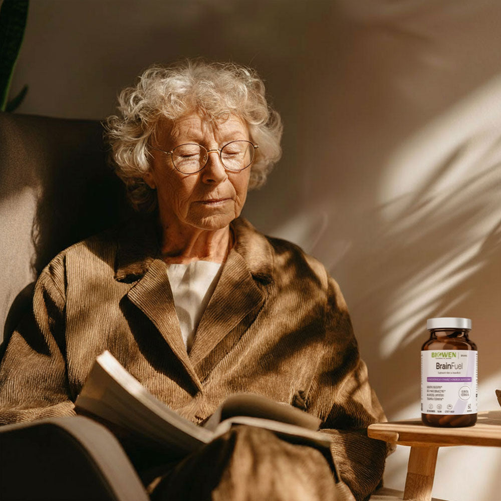 Starsza kobieta czytająca książkę w fotelu z butelką BrainFuel Biowen na stoliku obok