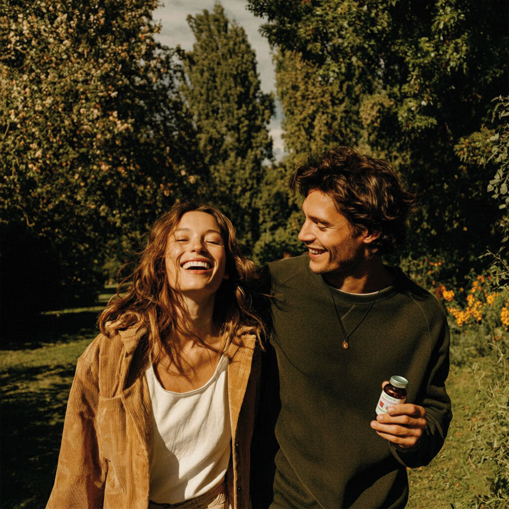 Kobieta i mężczyzna spacerujący w parku, mężczyzna trzyma Witamina D3 + K2 Biowen 90 kapsułek.