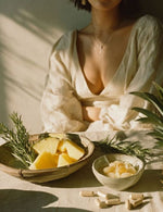 Kobieta w jasnej bluzce przy stole z kawałkami ananasa, rozmarynem i leżącymi kapsułkami EnzyMax Complex+.