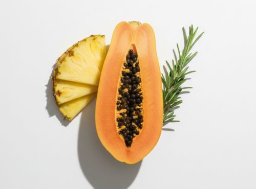 Połówka papai z pestkami, plaster ananasa i gałązka rozmarynu ułożone na białym tle.