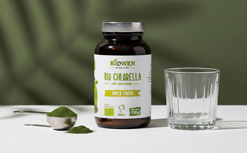 Słoiczek Bio Chlorella Biowen 120 g obok szklanki i miarki z zielonym proszkiem.