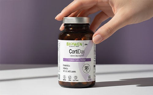 Dłoń trzymająca butelkę suplementu CortiDay Biowen 60 kapsułek ustawioną na gładkiej powierzchni