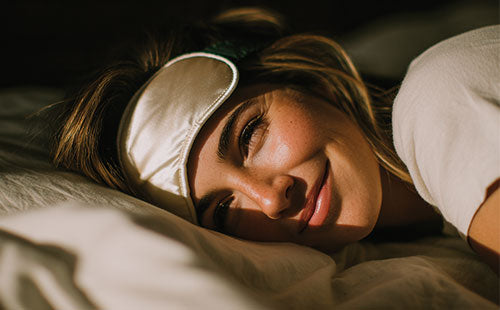 Zbliżenie kobiety odpoczywającej w pościeli z opaską na oczy w ciepłym świetle dnia.