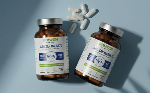 Dwa słoiczki Jabłczanu magnezu Biowen i kilka białych kapsułek na niebieskim tle.