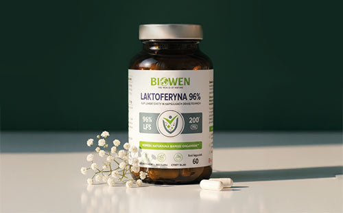 Słoiczek Biowen Laktoferyna 96% 60 kapsułek z białymi kwiatami i dwiema kapsułkami na jasnym tle.