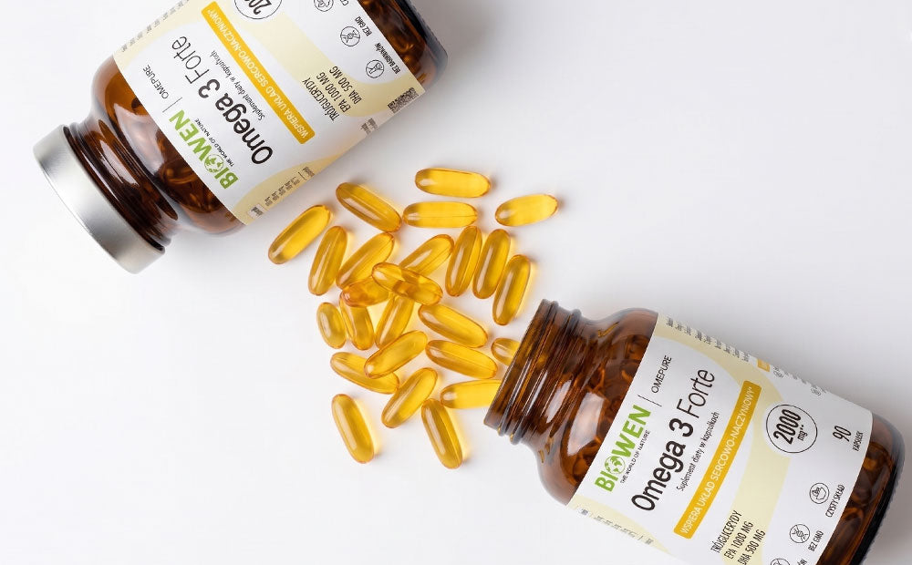 Kapsułki Omega 3 Forte Biowen rozsypane obok dwóch opakowań suplementu z kwasami omega-3 EPA i DHA