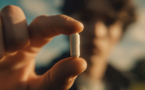 Zbliżenie na dłoń trzymającą kapsułkę Biowen z rozmytym tłem i sylwetką osoby.