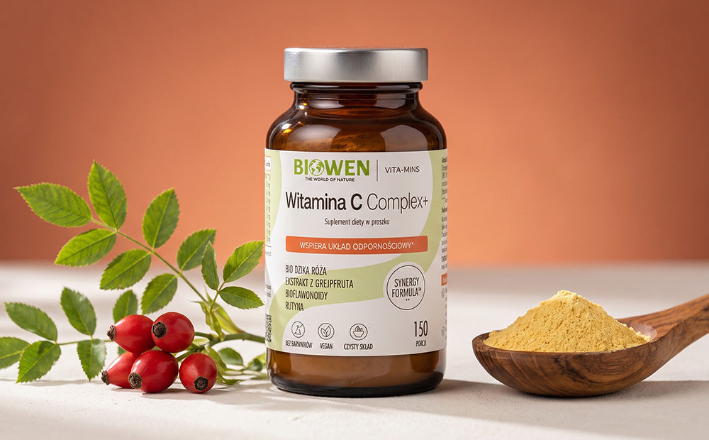 Witamina C Complex+ Biowen 150 g, suplement diety w proszku z dziką różą, ekstraktem z grejpfruta, bioflawonoidami i rutyną, obok drewnianej łyżki z proszkiem.