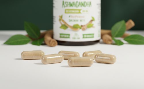 Zbliżenie na kapsułki Biowen Ashwagandha z widoczną etykietą słoiczka i elementami roślinnymi w tle.