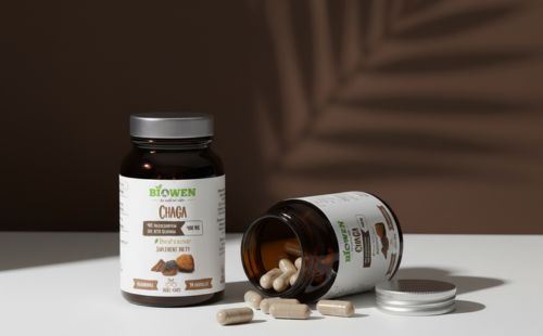 Suplement diety Biowen Chaga w kapsułkach w słoiczkach na jasnym tle z cieniem liścia