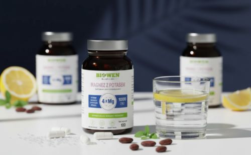Słoik suplementu Magnez z potasem Biowen 100 kapsułek obok szklanki wody z cytryną i kapsułek na białym tle.