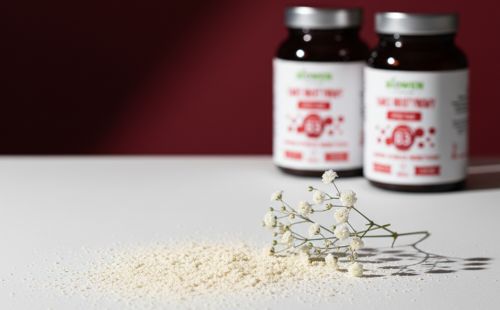 Proszek i gałązka białych kwiatów na jasnym blacie, w tle dwa słoiczki Niacyna (witamina B3) Biowen 120 g.