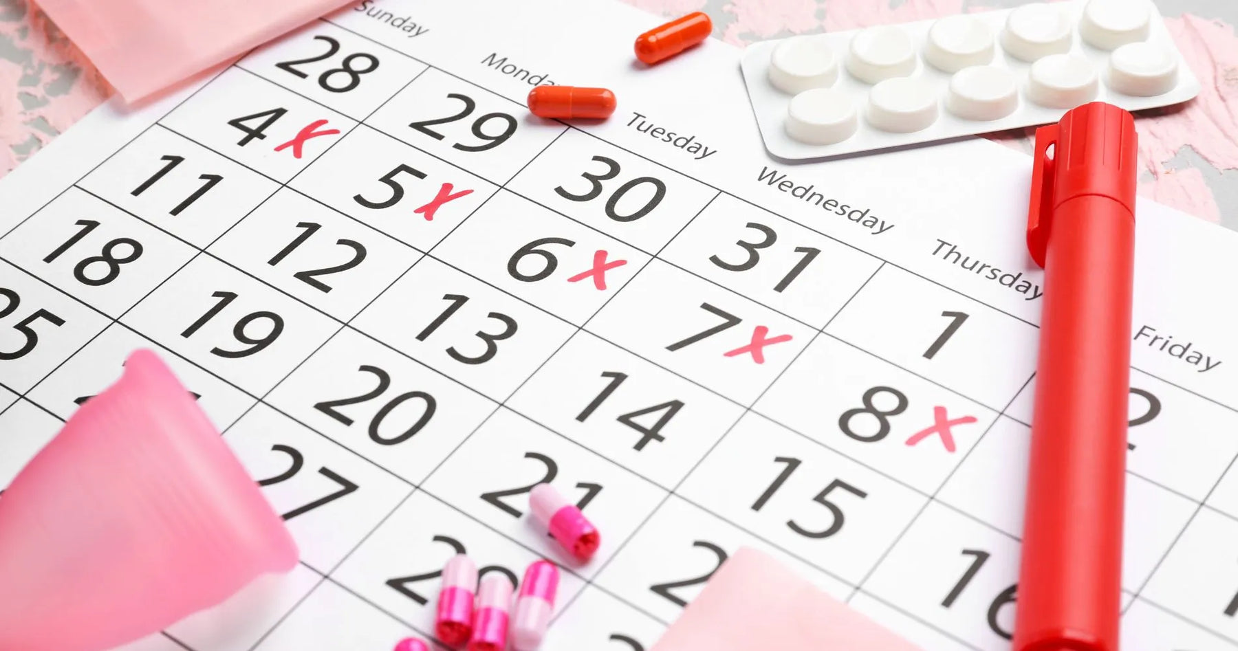 Kalendarz z zaznaczonymi datami cyklu menstruacyjnego, otoczony tabletkami i artykułami higienicznymi.