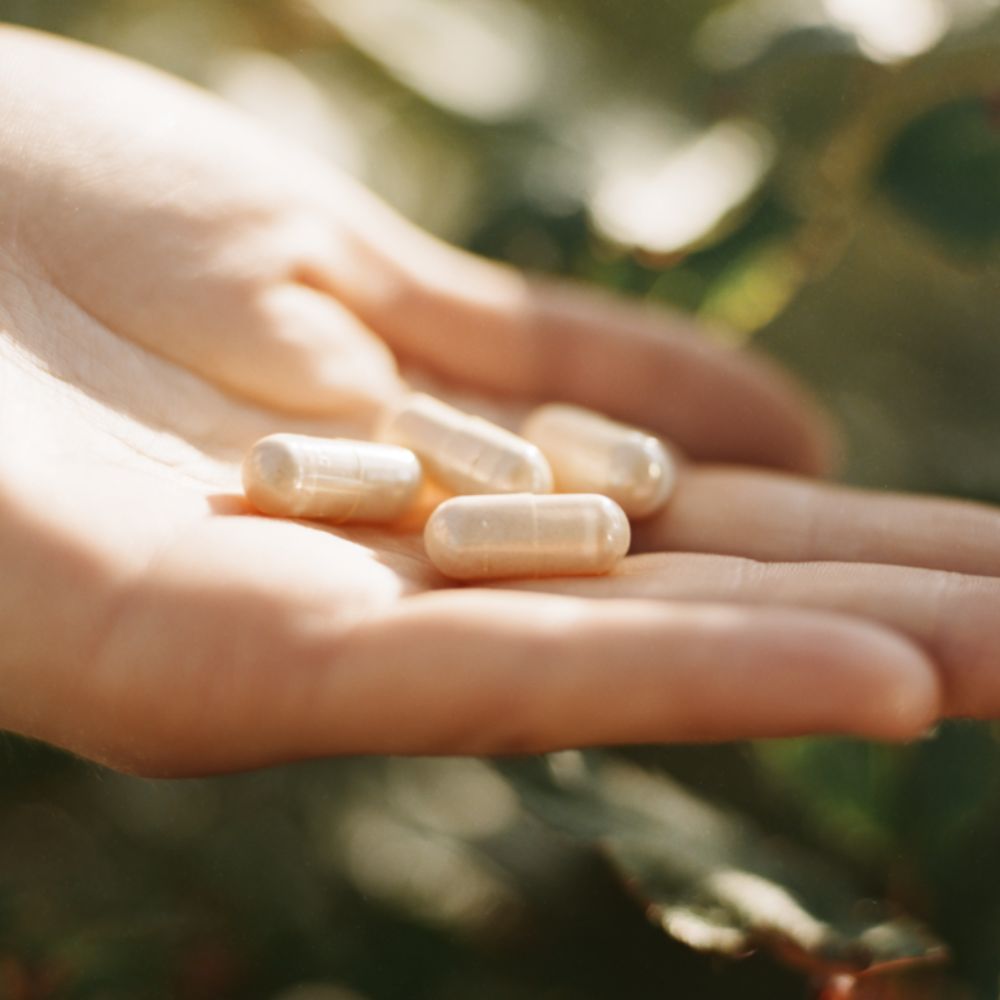 Dłoń trzymająca kilka białych kapsułek suplementu Magnez z potasem Biowen w naturalnym świetle.