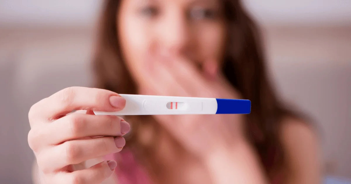 kobieta trzymająca test ciążowy zasłaniająca otwarte usta ręką 