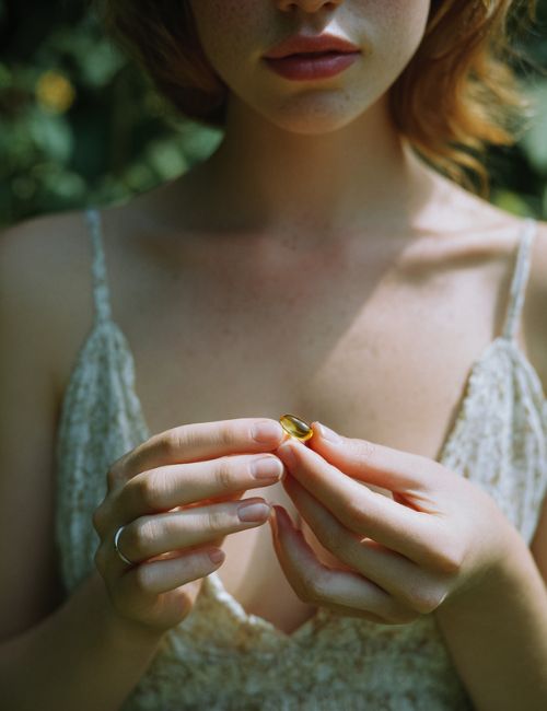 Kobieta w koronkowej sukience trzyma w dłoniach kapsułkę suplementu Ogórecznik Forte Biowen na tle zieleni.