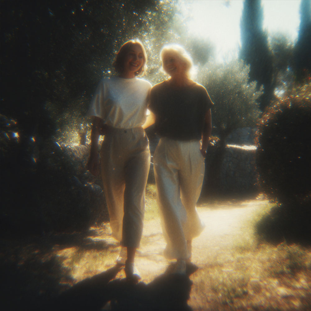 Dwie kobiety idące razem alejką w otoczeniu drzew i krzewów w słoneczny dzień.