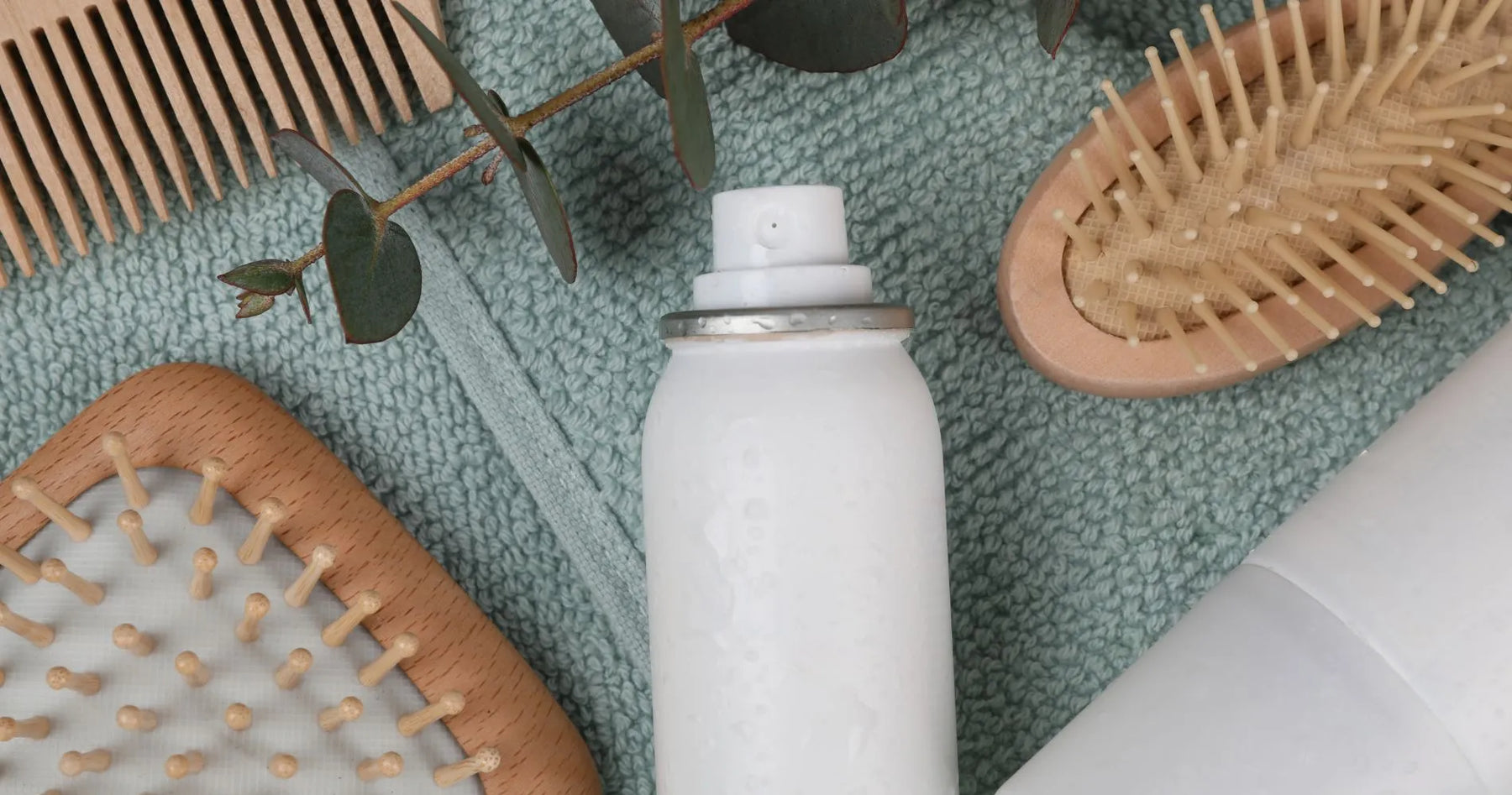 Suchy szampon w sprayu oraz drewniane szczotki do włosów na tle materiału – pielęgnacja włosów bez użycia wody.