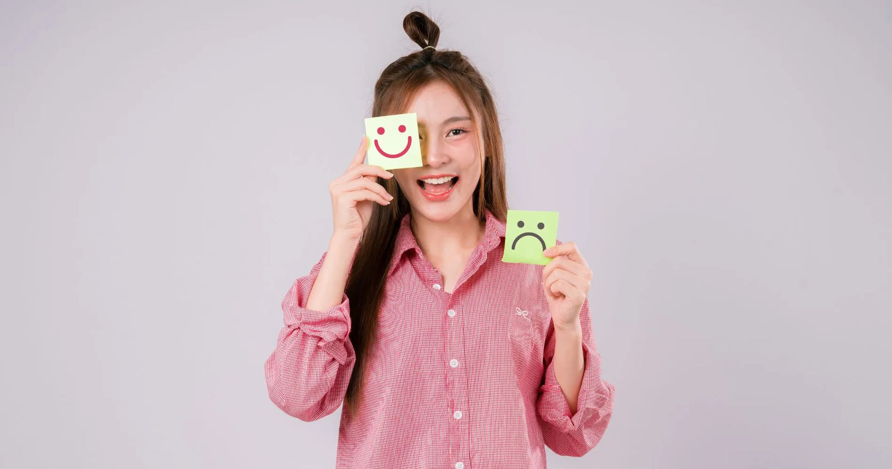 Kobieta trzymająca karteczki z uśmiechniętą i smutną buźką – symbol wpływu tryptofanu na nastrój i samopoczucie.