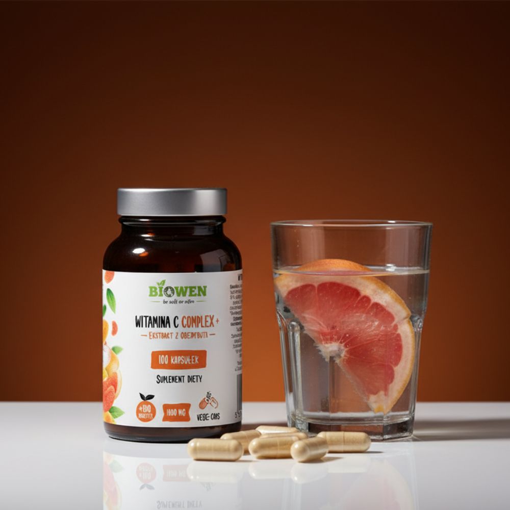 Biowen Witamina C Complex+ 100 kapsułek ustawiony przy szklance wody z kawałkiem grejpfruta.