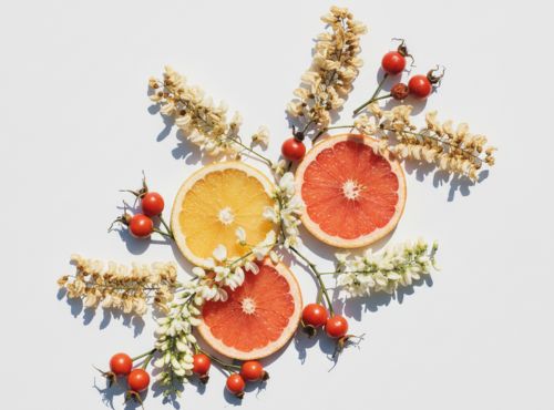 Plastry czerwonego i żółtego grejpfruta z owocami dzikiej róży i białymi kwiatami na jasnym tle.