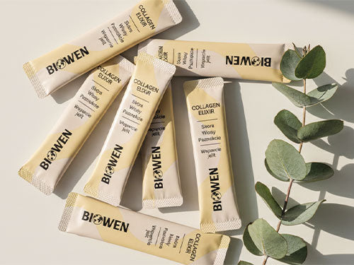 Kilka beżowych saszetek Biowen Collagen Elixir z napisem marki ułożonych artystycznie na białym tle z dekoracją z zielonych gałązek eukaliptusa